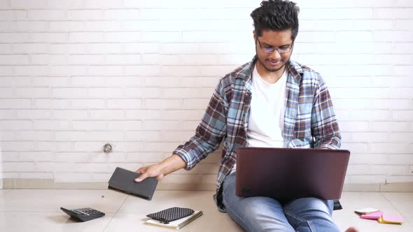 Young Man in Casual Dress Sitting on Floor Working on Laptop alt
