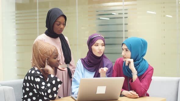 Muslim Asian and African Women in Hijabs Sit in Cafes and Make Online Purchases Using a Laptop