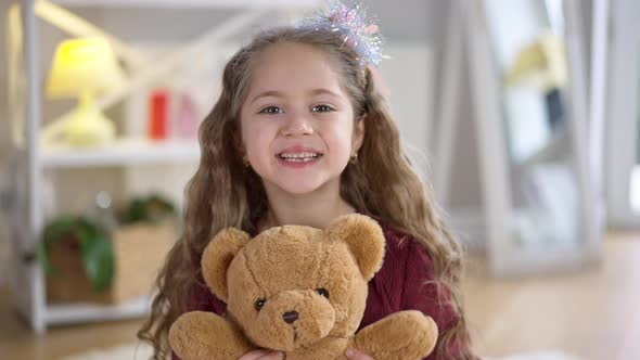 Closeup Portrait of Charming Little Girl Holding Teddy Bear Looking at Camera Smiling alt