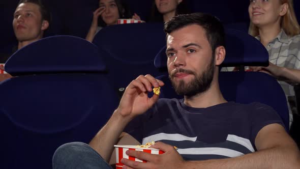 Attractive Young Man Eating Popcorn During Boring Movie at the Cinema alt
