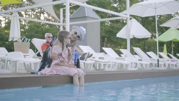 Grandmother Hugs Her Granddaughter Sitting By the Pool and Look at the Camera alt
