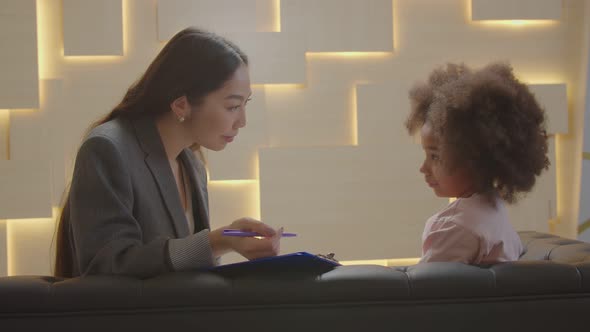 Asian Woman Counselor and Cute Little African Girl Sharing During Psychotherapy alt