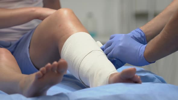 Traumatologist Wearing Elastic Bandage on Injured Patient Leg, Trauma Result