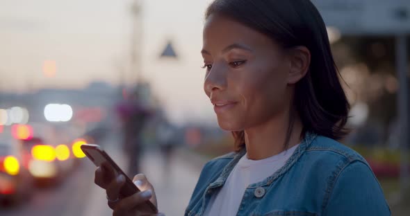 Bokeh Shot of Smiling Afro Woman Text Message on Cellphone Outdoors alt