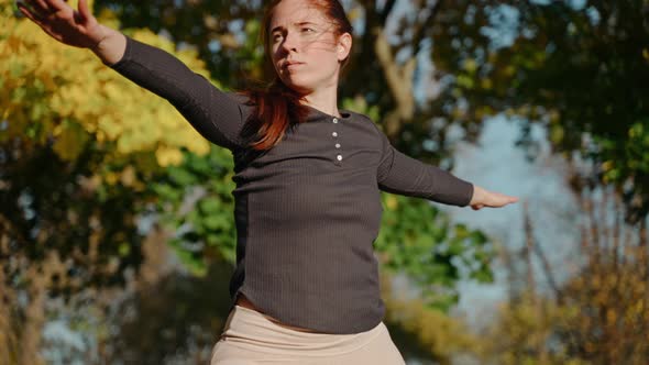 Close Shot of Young Woman Standing in Warrior Pose in Autumn Park on a Yoga Mat