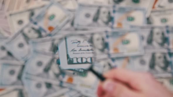 Lot of One Hundred Dollars Bills Inspecting Under Magnifying Glass alt