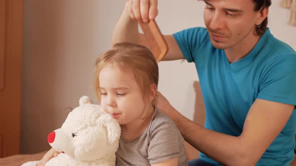 Dad Combs His Daughter's Hair Little Baby Girl on Bed in Bedroom