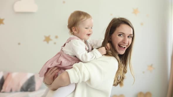 Happy Mom Rolls Her Little Daughter on Her Neck