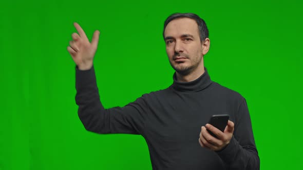 Man Holds the Phone in His Hands and Points to the Side on Isolated Green Background alt