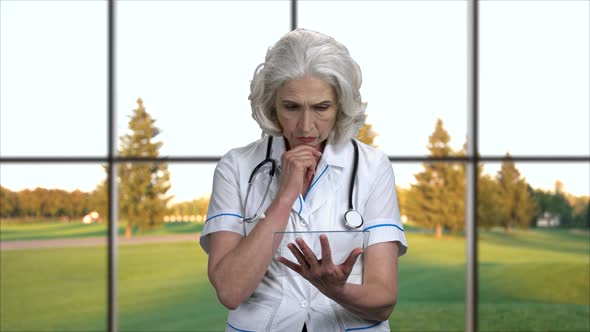 Confident Mature Doctor Using Transparent Tablet Device. alt
