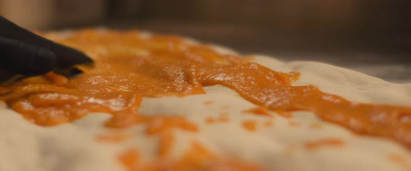 Chef spreading special pumpkin sauce over a fresh pizza al taglio dough. Close up, slow motion. alt