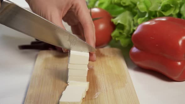 A Woman Cuts Feta Cheese on a Wooden Board with a Large Sharp Knife to Make a Greek Salad