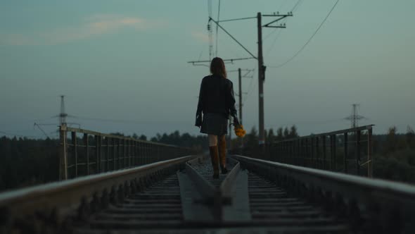 Young Beautiful Rebel Woman with Yellow Flowers Walks Along the Railway