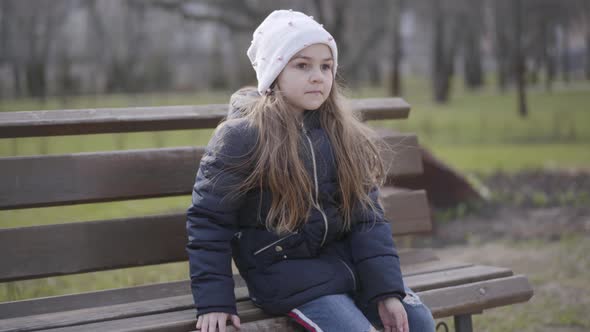 Brunette Schoolgirl Sitting on Bench in Park and Raising Leg. Portrait of Lonely Sportive Kid alt