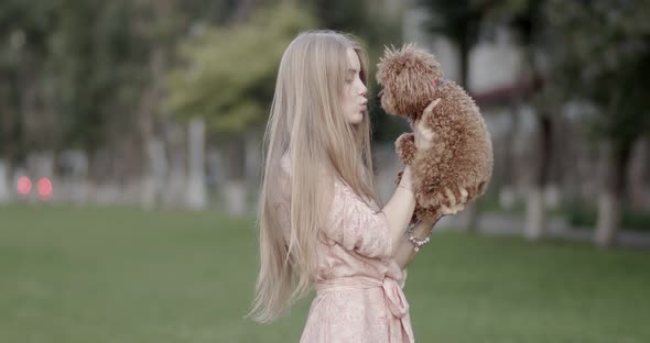 A beautiful girl, blonde, is holding a poodle dog in her hands