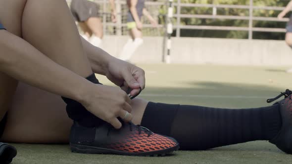 Side View of Female Football Player Lacing Up Shoes at Stadium alt