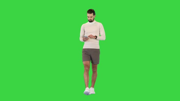 Male Runner Walking and Typing Something on His Mobile Smart Phone on a Green Screen Chroma Key alt