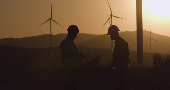 Engineers Review Information in Tablet, Turning Head Towards Windmill at Sunset alt