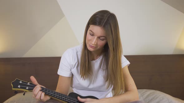 Young Woman Learning To Play The Ukulele Using Laptop at Home, Distance Learning Online Education