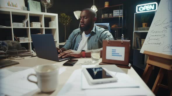 Overworked African American Man Finishing Project in Hipster Coworking. alt