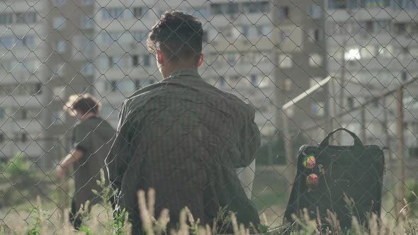 Back View of African American Man Sitting Behind Mesh Fence and Looking at Guys Playing Football alt