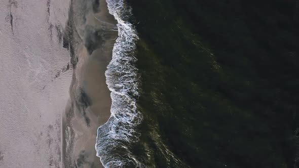 Moving forward drone shot of the seaside with waves crashing on the beach alt