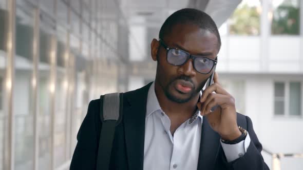 African Confident Businessman in Glasses Talking on Mobile Phone Outside alt