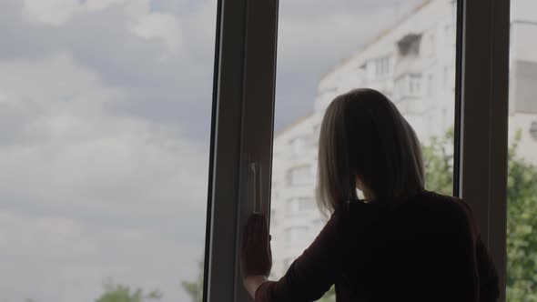 Back View A Woman Washes a Window in the Apartment of a Highrise Building alt