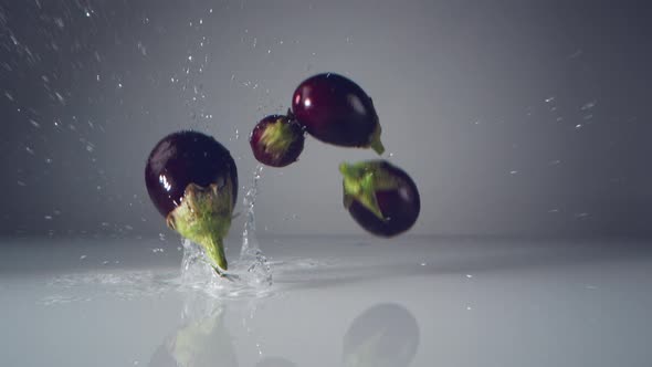 Fresh eggplants falling on water surface. Slow Motion. alt