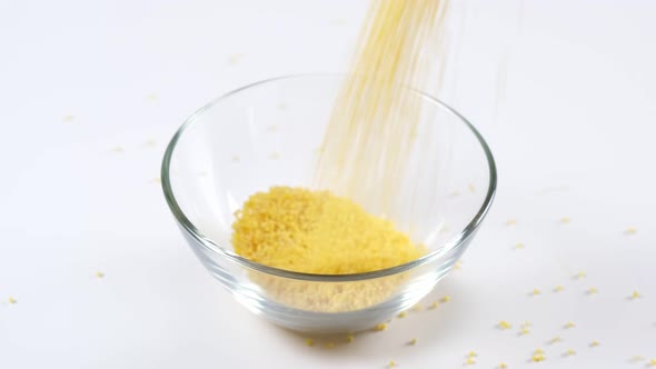 Millet falling in a glass bowl on white background. Healthy organic food diet concept.