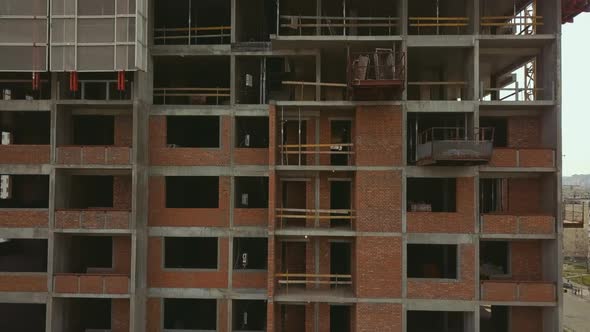 Raising the Camera Up Along a Building Under Construction with Empty Floor Spans and Workers on the