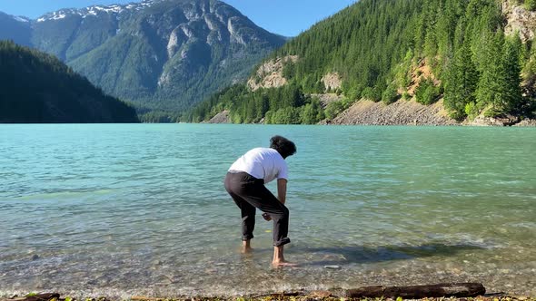 Man throwing a stone into crystal clear water. Snow Lake, Washington. In the background a snowy moun alt
