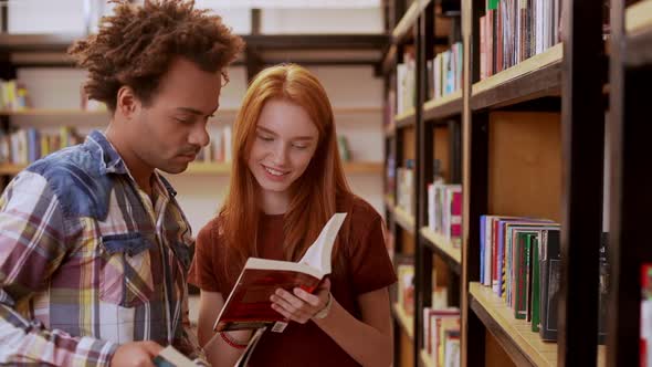 Beautiful Teenage Foxy Girl in Library Discussing Books with African American Guy with Afro Haircut alt