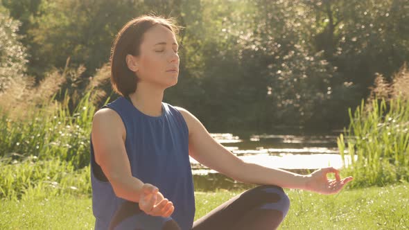 Young woman doing yoga exercise in green park, meditating in summer sunny morning. alt