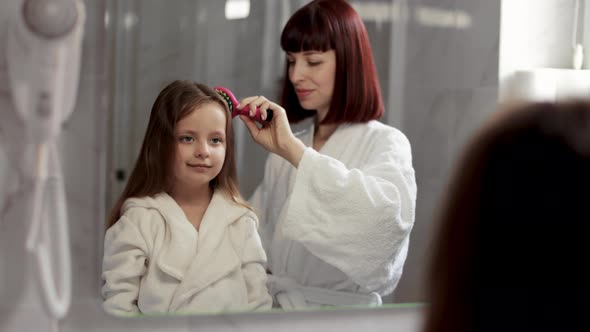 Loving Mom Brushing Hair of Cute Little Girl in the Bathroom alt