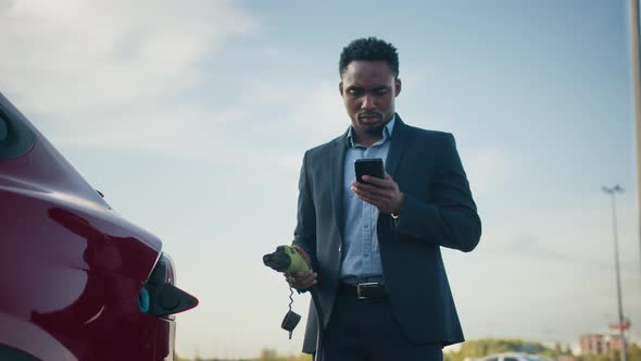 Close Up of African Businessman Unplugging Charging Cable From Electric Car alt