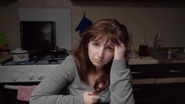 Boring Woman Sitting in the Kitchen in the Evening and Looking at the Camera