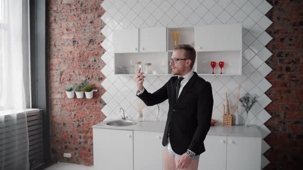 Man Standing in Kitchen Wearing Suit and Having Formal Business Video Call Through Smartphone.
