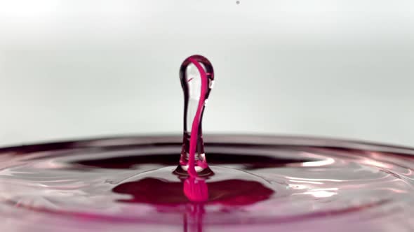Pink droplet of paint splashing into liquid and bouncing up alt