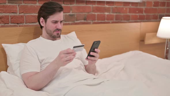 Casual Young Man with Unsuccessful Online Payment on Smartphone in Bed alt