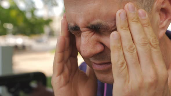 Closeup of a Man Massaging His Temples As a Result of a Headache Outside in a Park