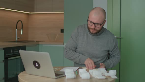Young Adult Man Counting Dollars for Home Budget with Store Receipts on the Table alt
