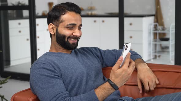 Happy Young Bearded Indian Eastern Man Holding Cellphone and Making Video Call alt