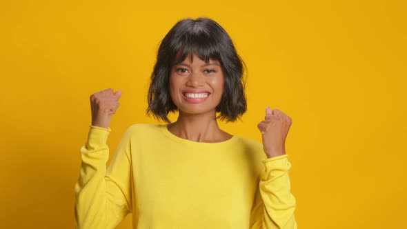 Happy Woman Makes Fist Pump with Triumph Celebrates Success on Yellow Background alt