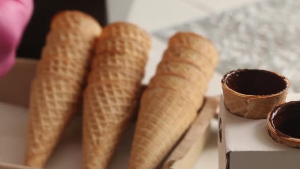 A Woman Smears Waffle Cones With Liquid Chocolate And Puts Them On The Counter. alt