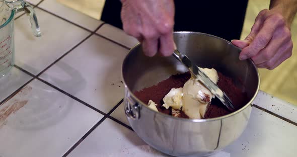 A chef in a kitchen putting vegan butter into a metal mixing bowl while baking a chocolate cake for alt