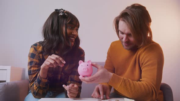 Happy Young Mutiethnic Couple Saving Coins in Their Piggy Bank alt