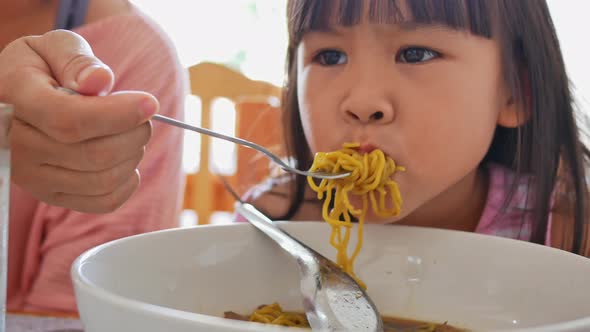 Mother feeds her lovely daughter Thai noodles in a restaurant. happy and healthy childhood concept alt