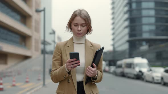 Business Woman Carrying Clipboard and Using Mobile on Street alt