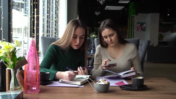 Two Young Businesswomen Sit Together in a Cafe and Talk on the Phone